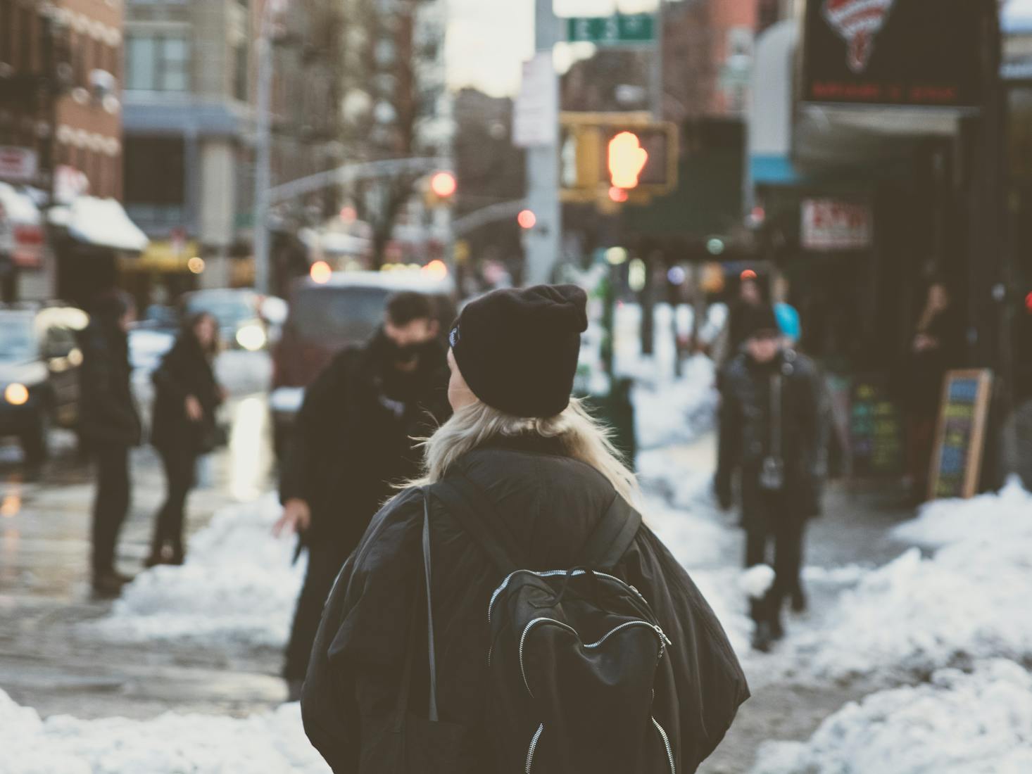 The back of a person carrying a backpack through the East Village streets in the snow