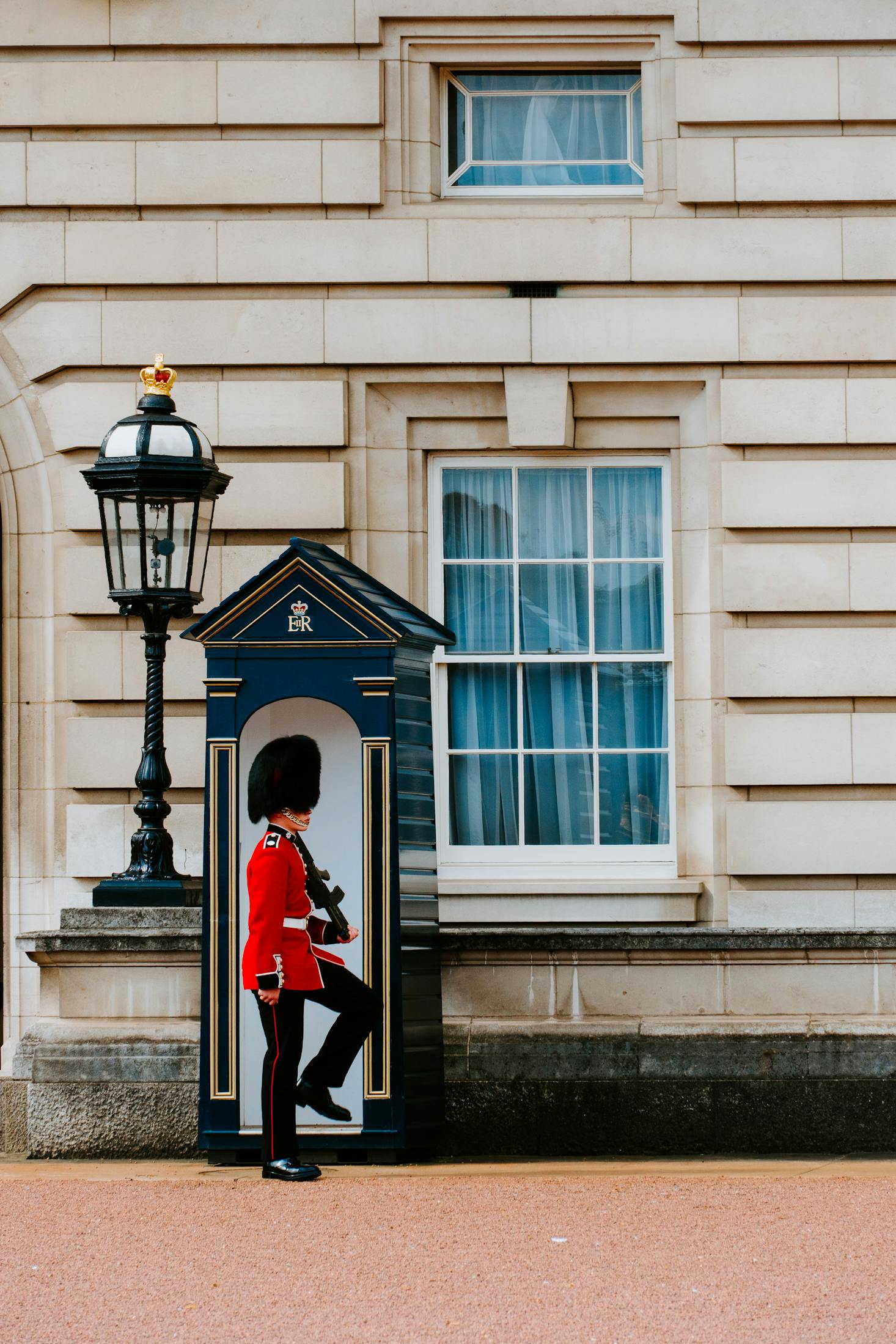 A guard dressed in red with a tall black hat in front of Buckingham Palace in London