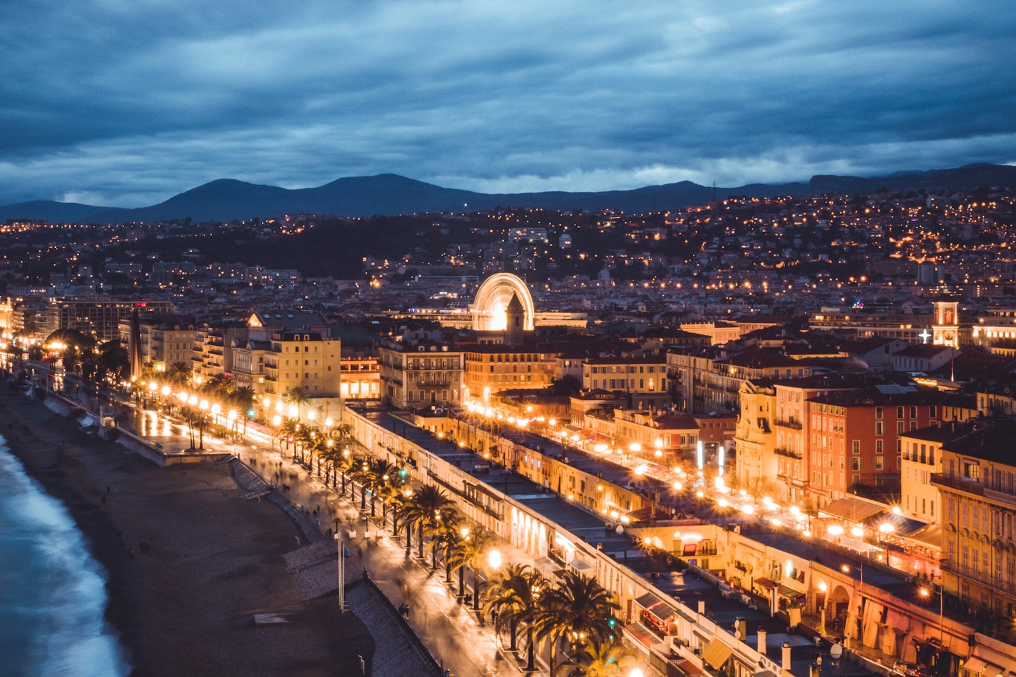 A view of the coastal lit-up Nice at night, stretching from the sea to the mountains in the distance