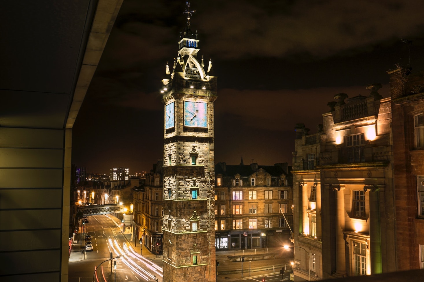 Glasgow Steeple, a clock tower, lit up at night surrounded by other buildings