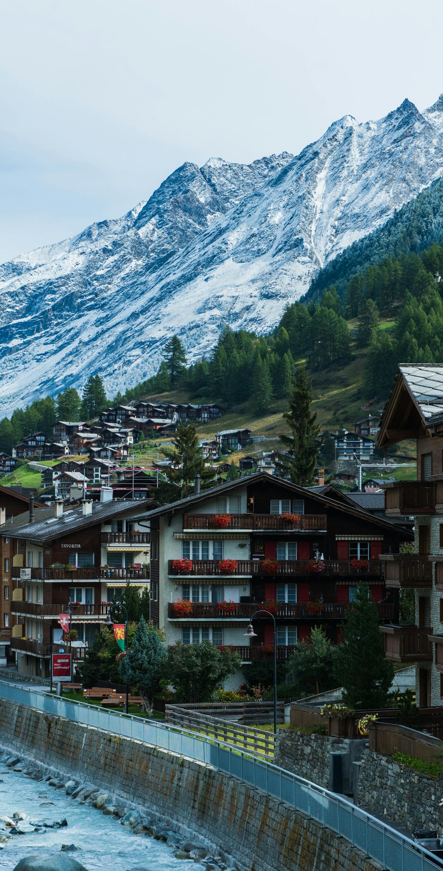 Alpine chalets line the green and snow-covered mountainside in Zermatt, Switzerland