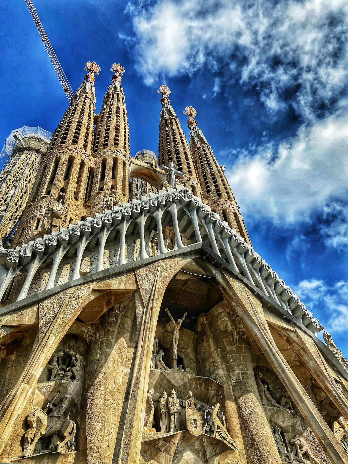 The intricate facade of Sagrada Familia in Barcelona with blue sky and white clouds behind it.