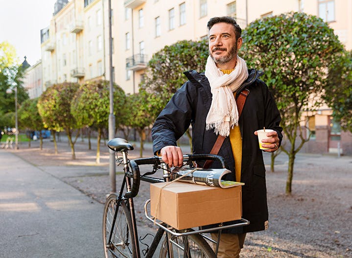 Mann schiebt ein Fahrrad, darauf liegt ein Karton aus Wellpappe