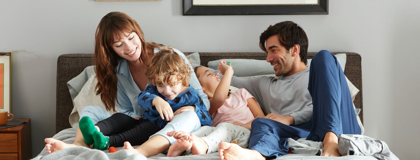 Family lounging on bed in a sunlit room.