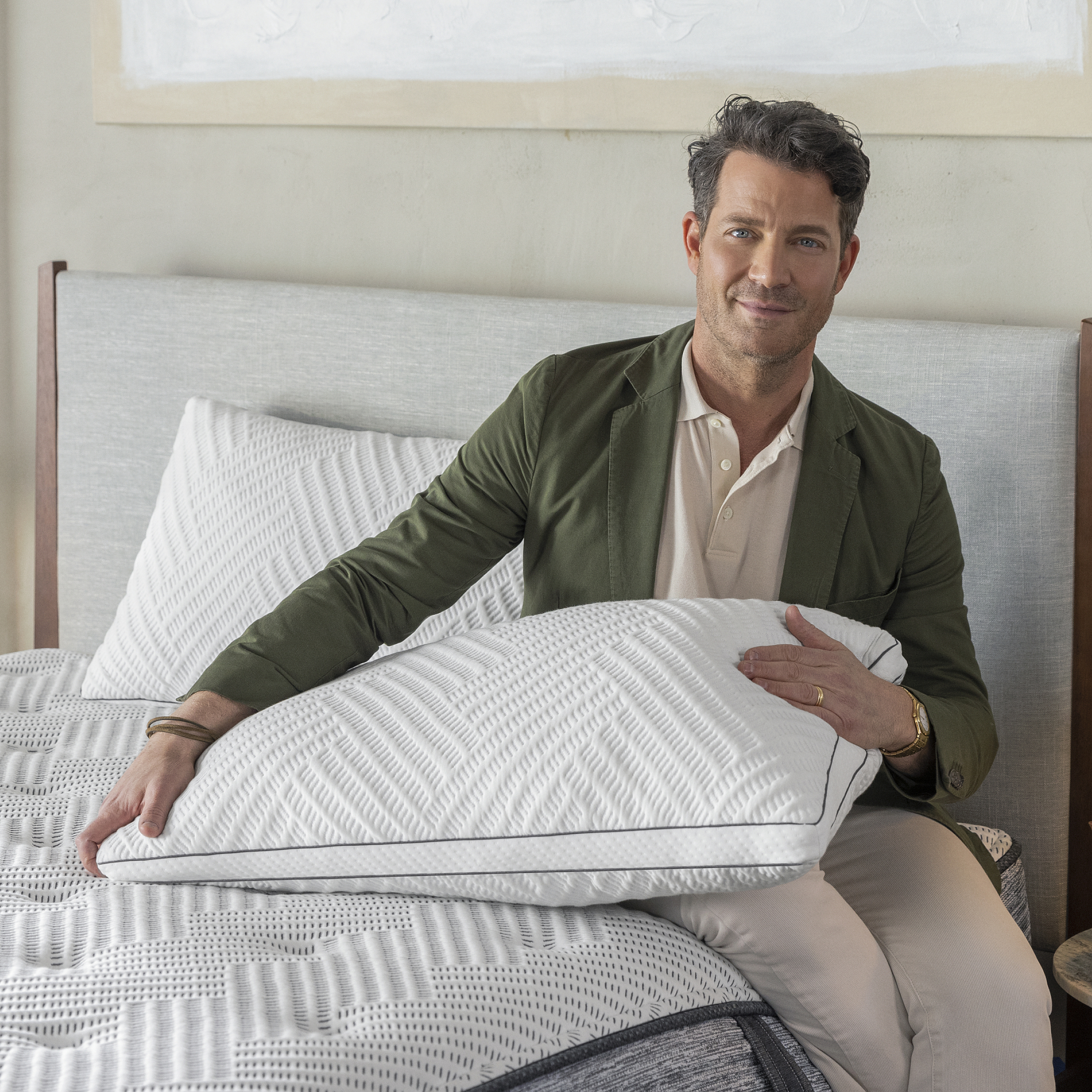 Nate Berkus sitting on the Beautyrest Nate Berkus Limited Edition Mattress holding the Nate Berkus Limited Edition Pillow