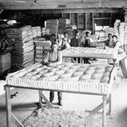 Black and white photo of people with mattresses in a warehouse