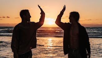 two men high-fiving on a beach during sunset