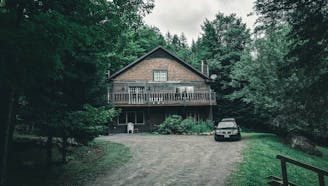 secluded brown brick home with a porch and car in driveway surrounded by a forest