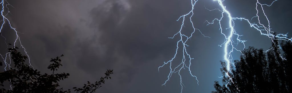 lightning across a dark, cloudy sky with trees