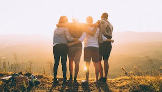 four friends holding each other's backs while looking into the sunset hiking