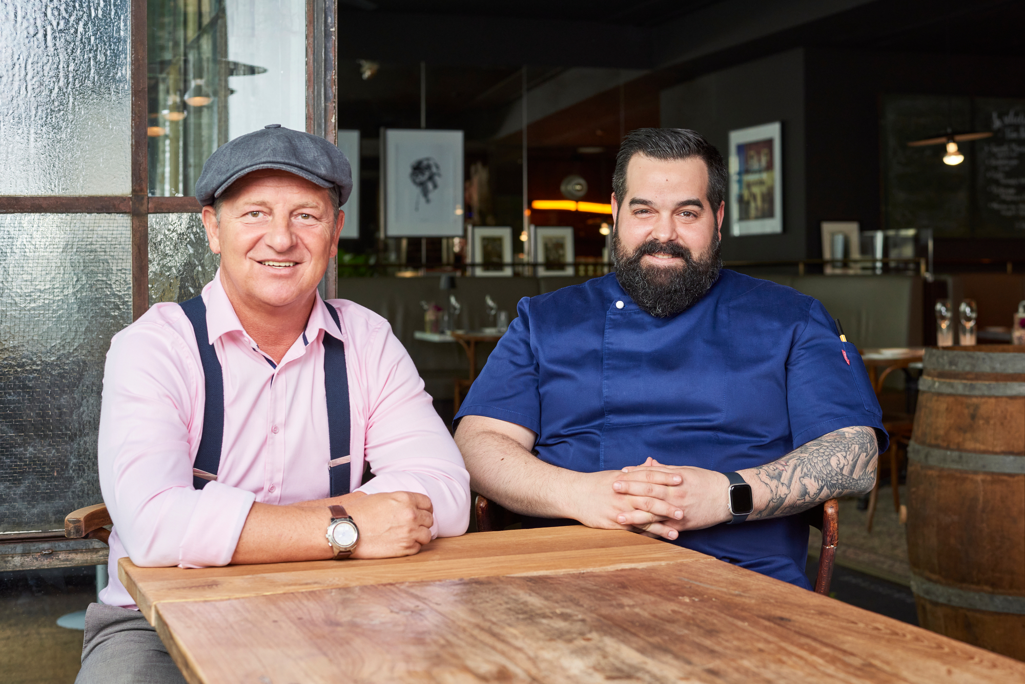 Zwei Männer sitzen an einem Tisch und blicken freundlich in die Kamera.