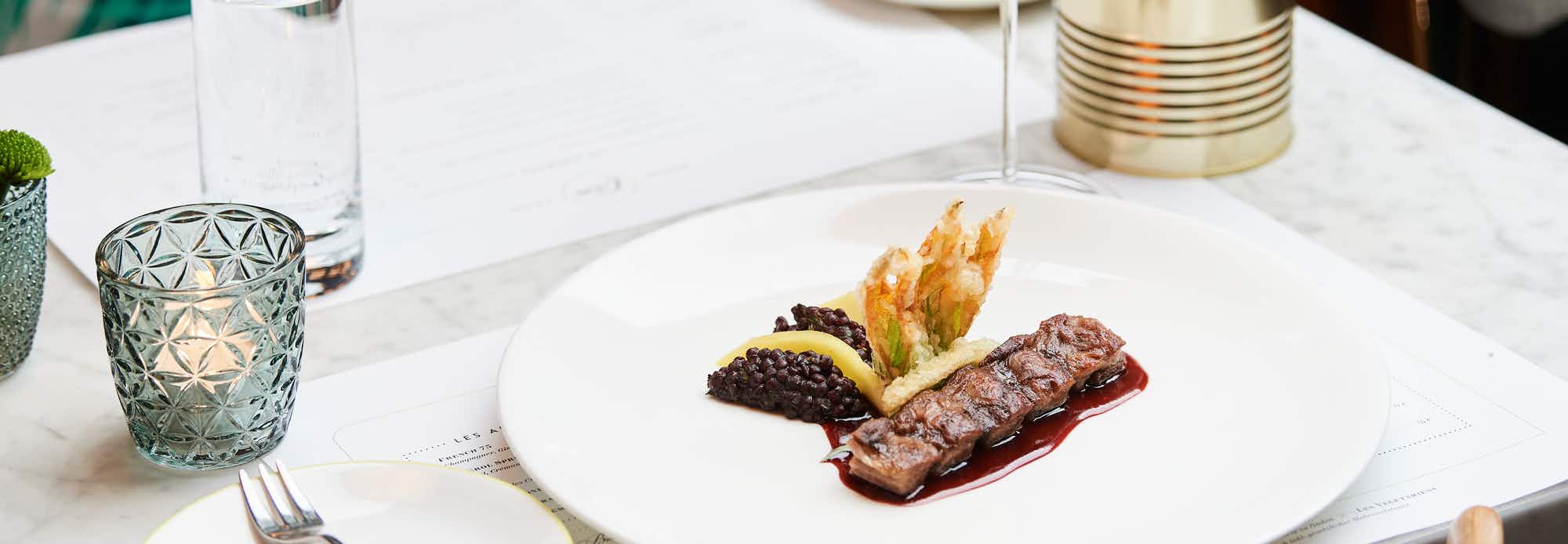 Gedeckter Tisch der Brasserie Colette Tim Raue: Tisch mit Fleischgericht und Rotweinglas