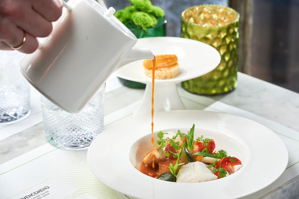 Angerichtete Speise: Bouillabaisse, Kellner gießt die Fischsuppe aus einem weißen Kännchen an