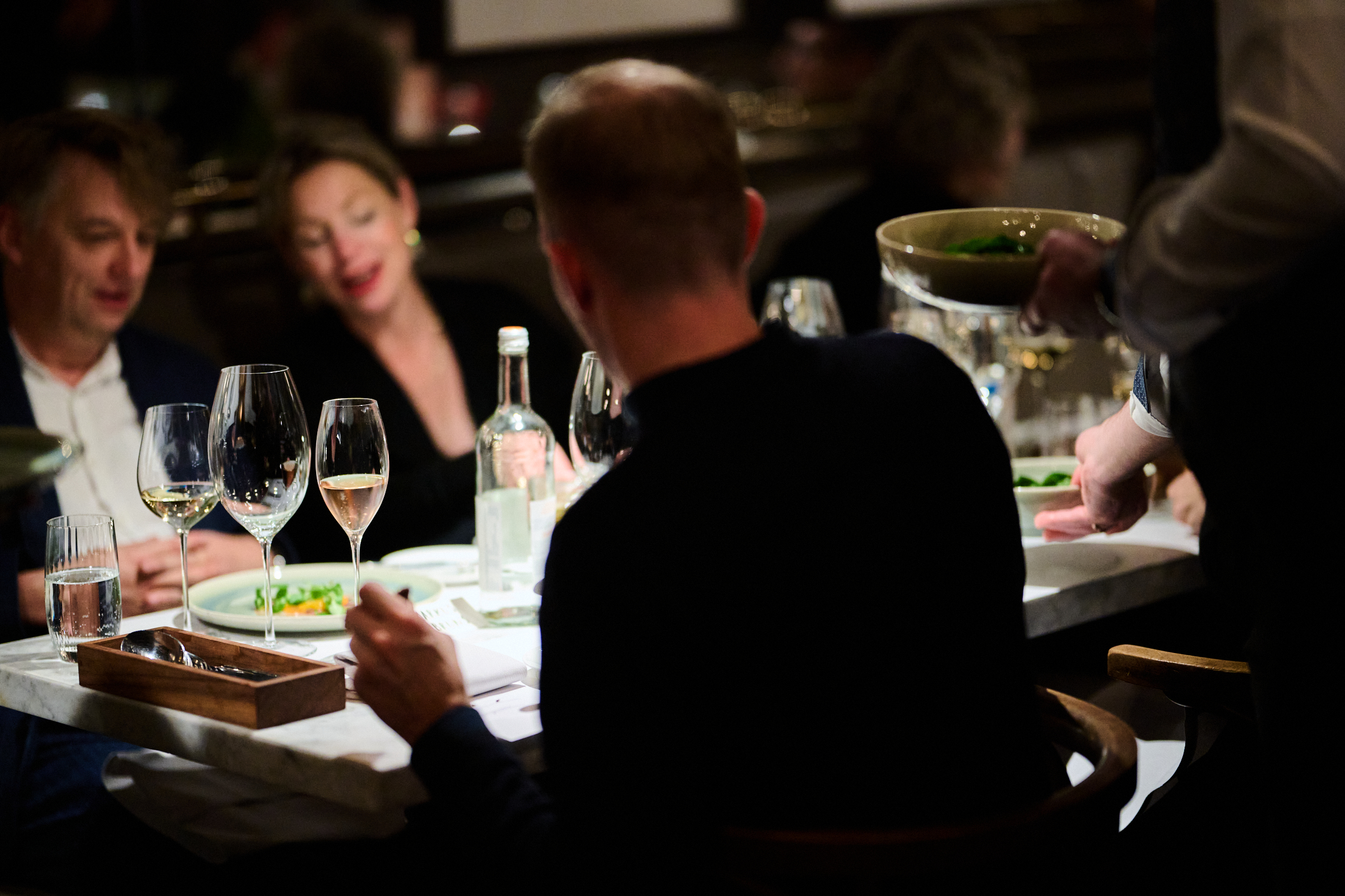 Szene am Restauranttisch, Gäste bei einem angeregten Gespräch, auf dem Tisch stehen Weingläser