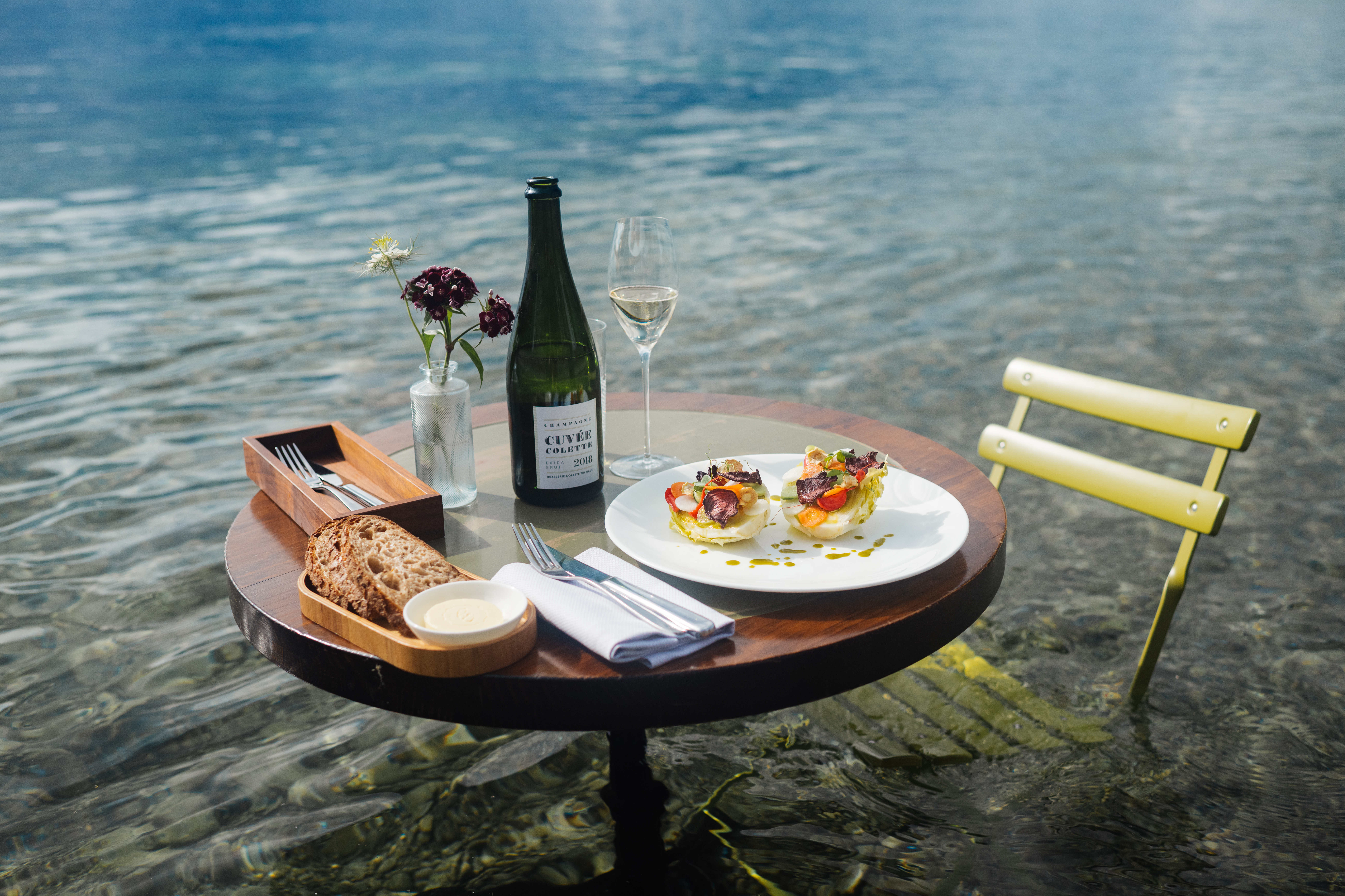 Bistrotisch mit Cuvée Flasche, Besteck und Teller auf dem Salatvariation