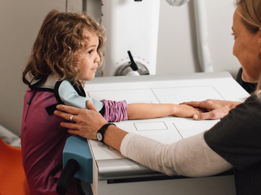 Medical assistant with hand on child's shoulder during x-ray imaging