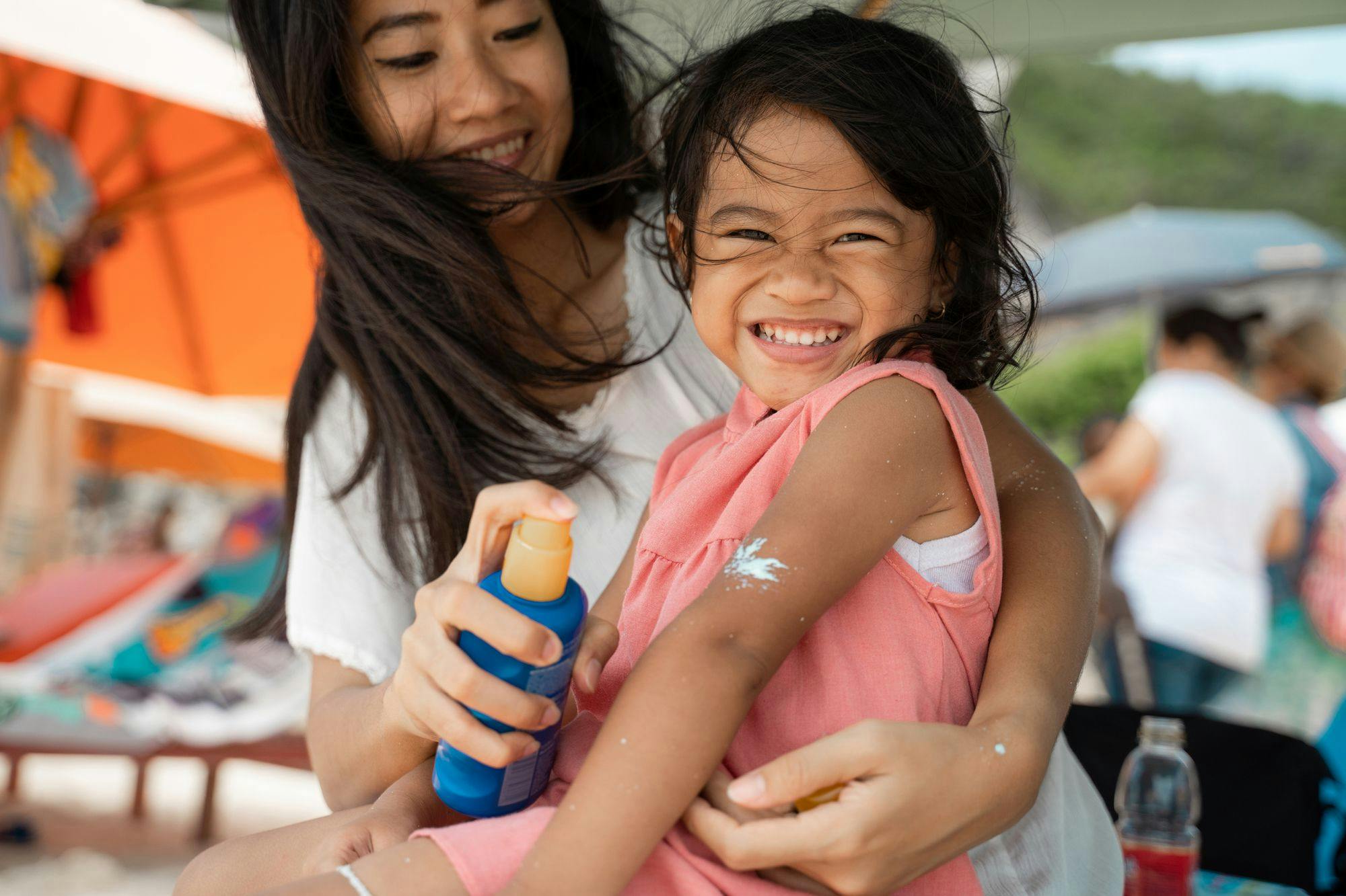 A parent sprays sunscreen onto a smiling child.