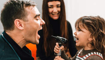 Child playfully holding otoscope with doctor and parent