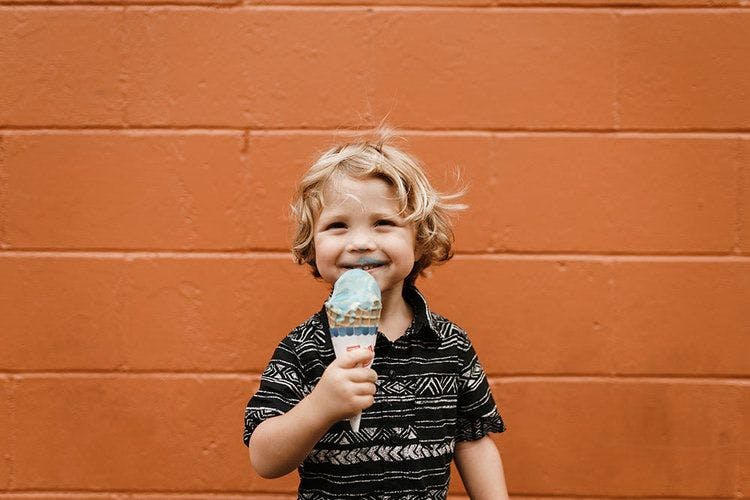 A young child smiles while holding an ice cream cone. 