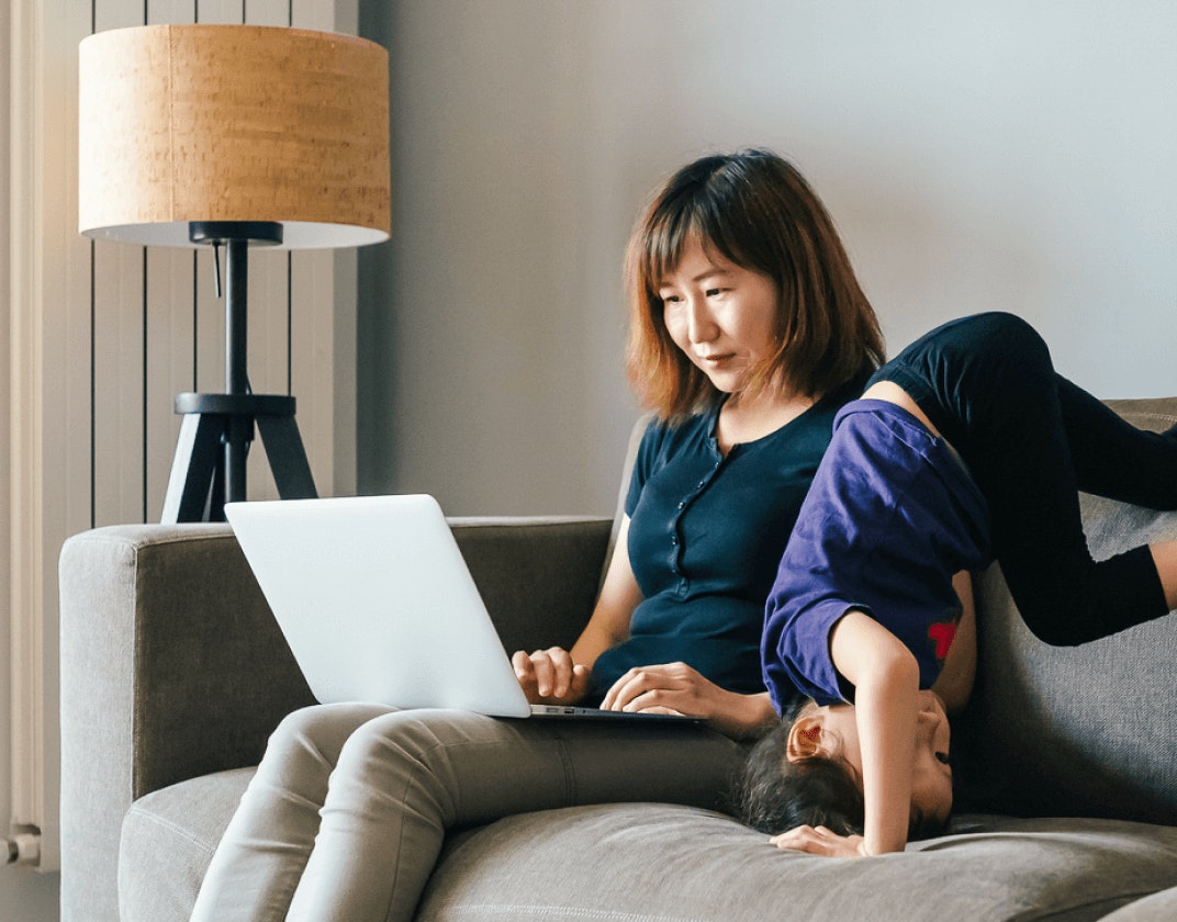 Child does headstand next to mom who is on her laptop