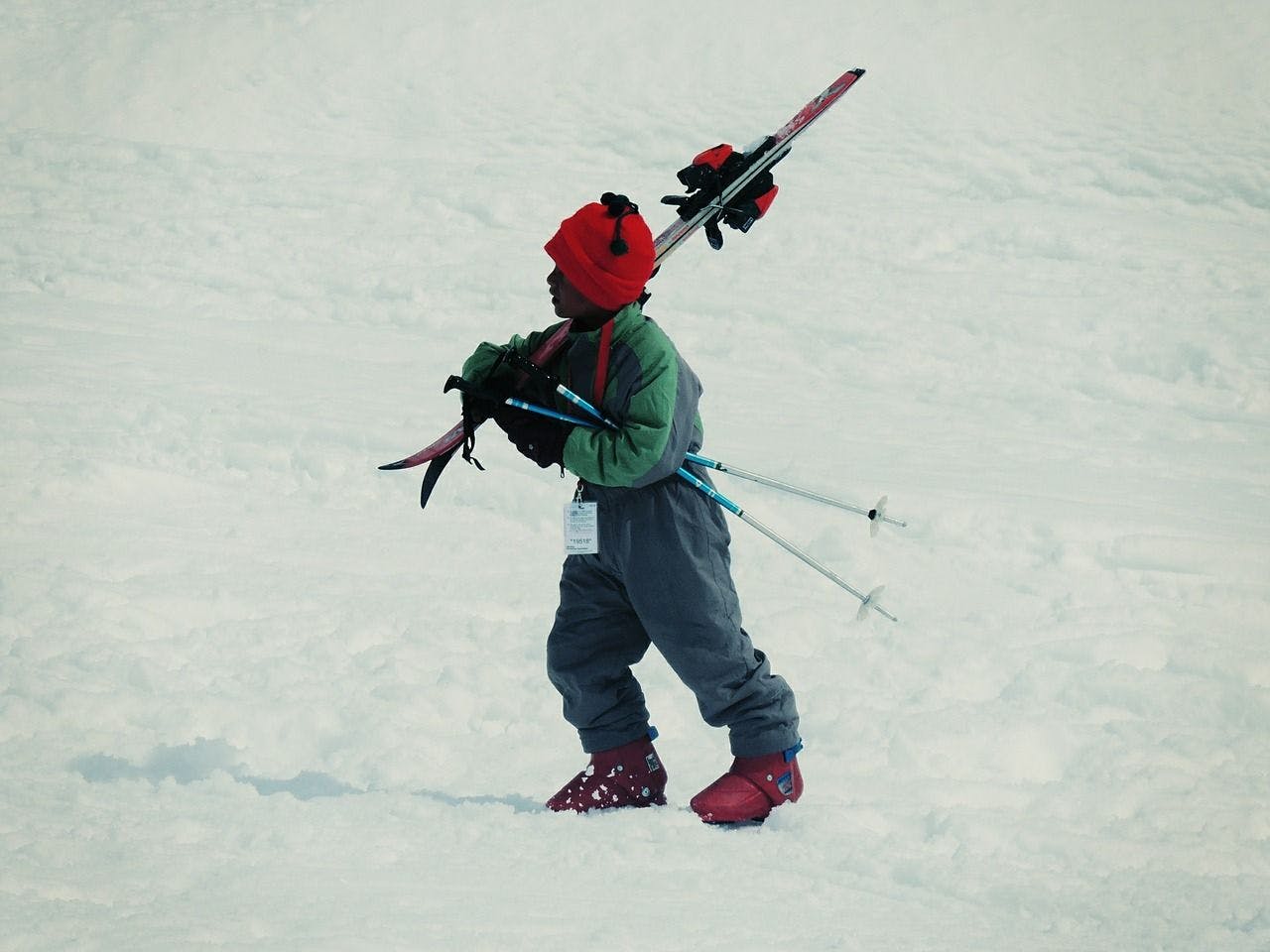 A child walks through the snow with skis. 
