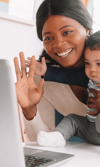 Mom holding a baby smiles and waves at someone on the computer screen