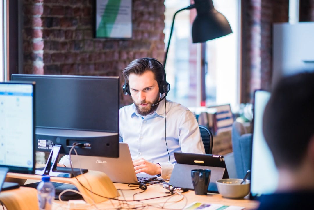 Man with a headset sitting in front of a laptop in office. approachable, friedly team, support