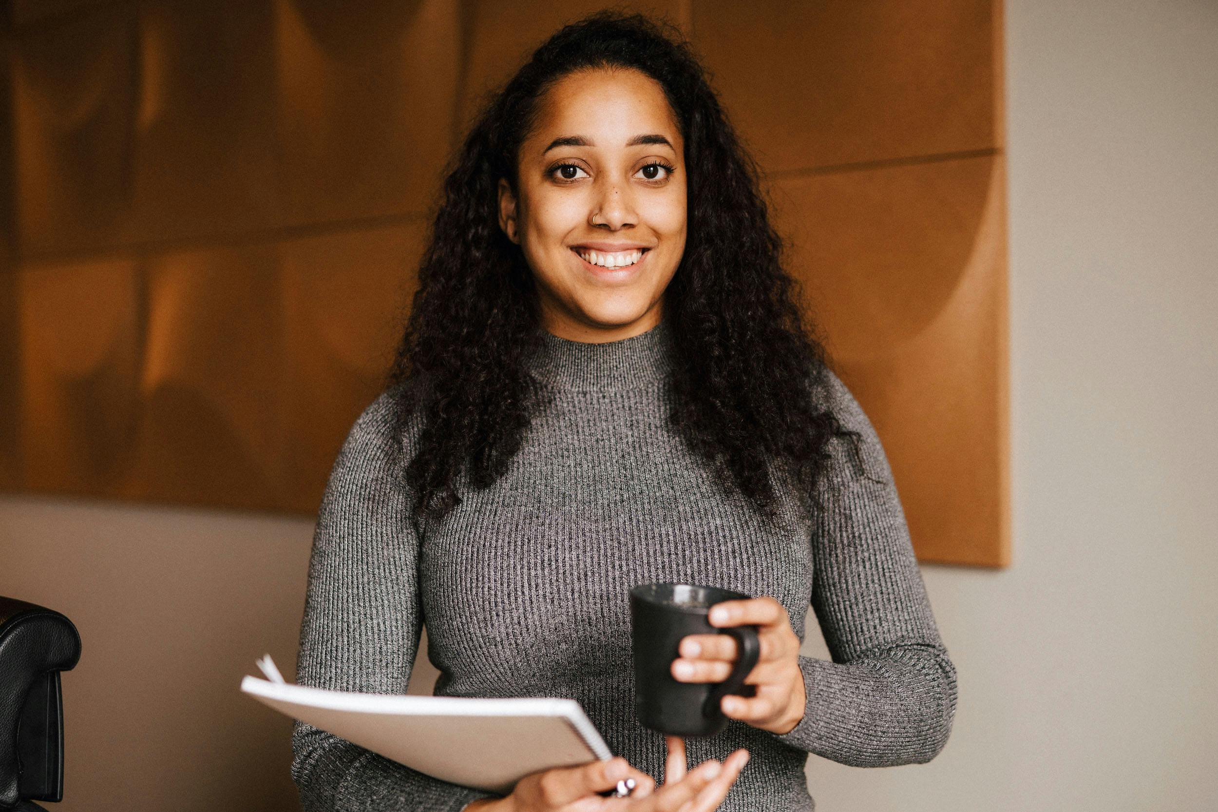 Woman smiling. Holding a coffee cup and a note book
