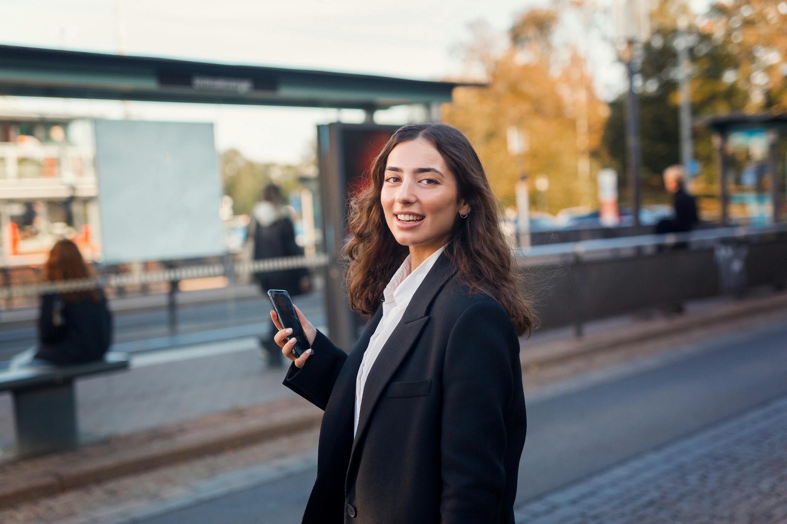 Person med mobiltelefon vid busshållplats.