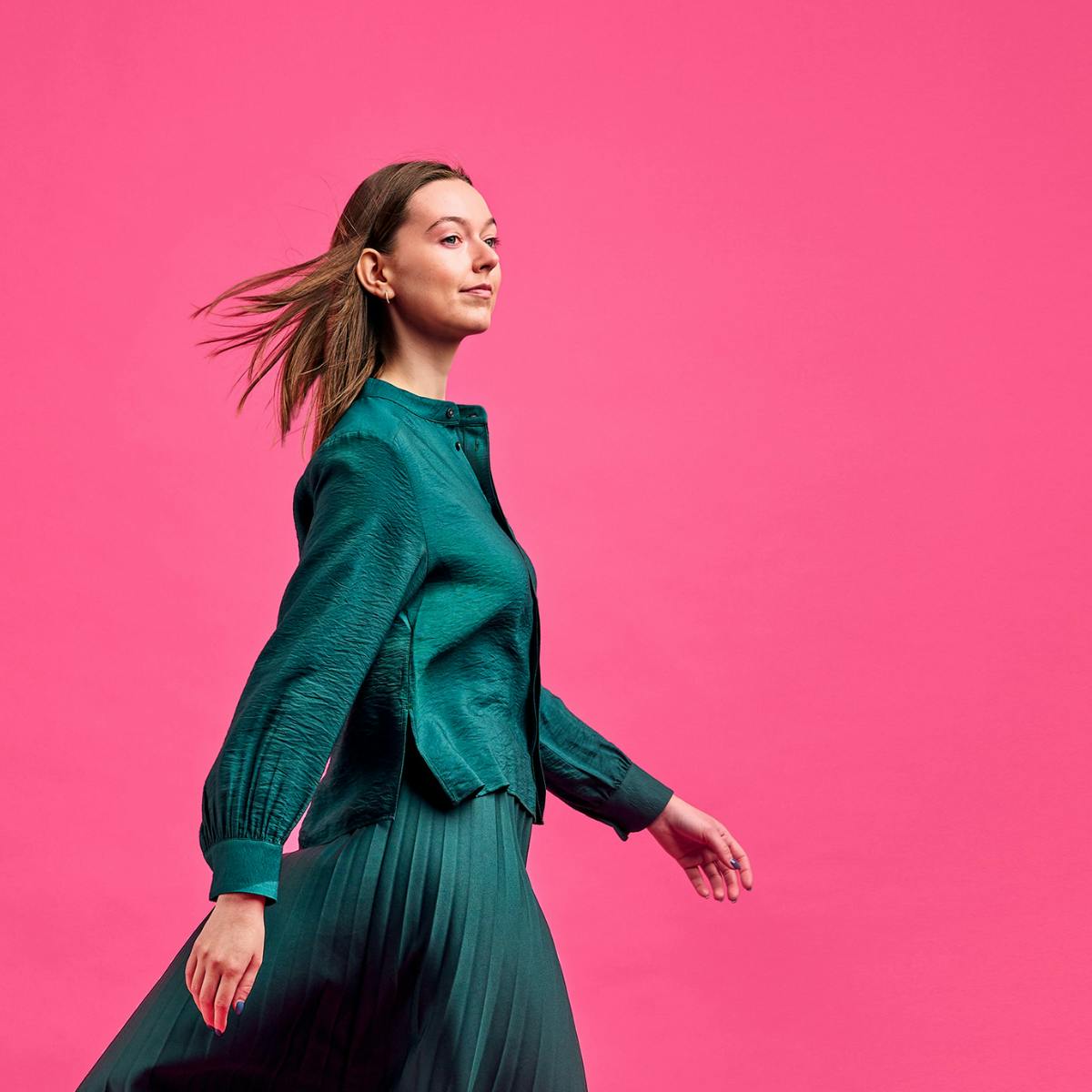 En person i grön blus och kjol. Rosa bakgrund