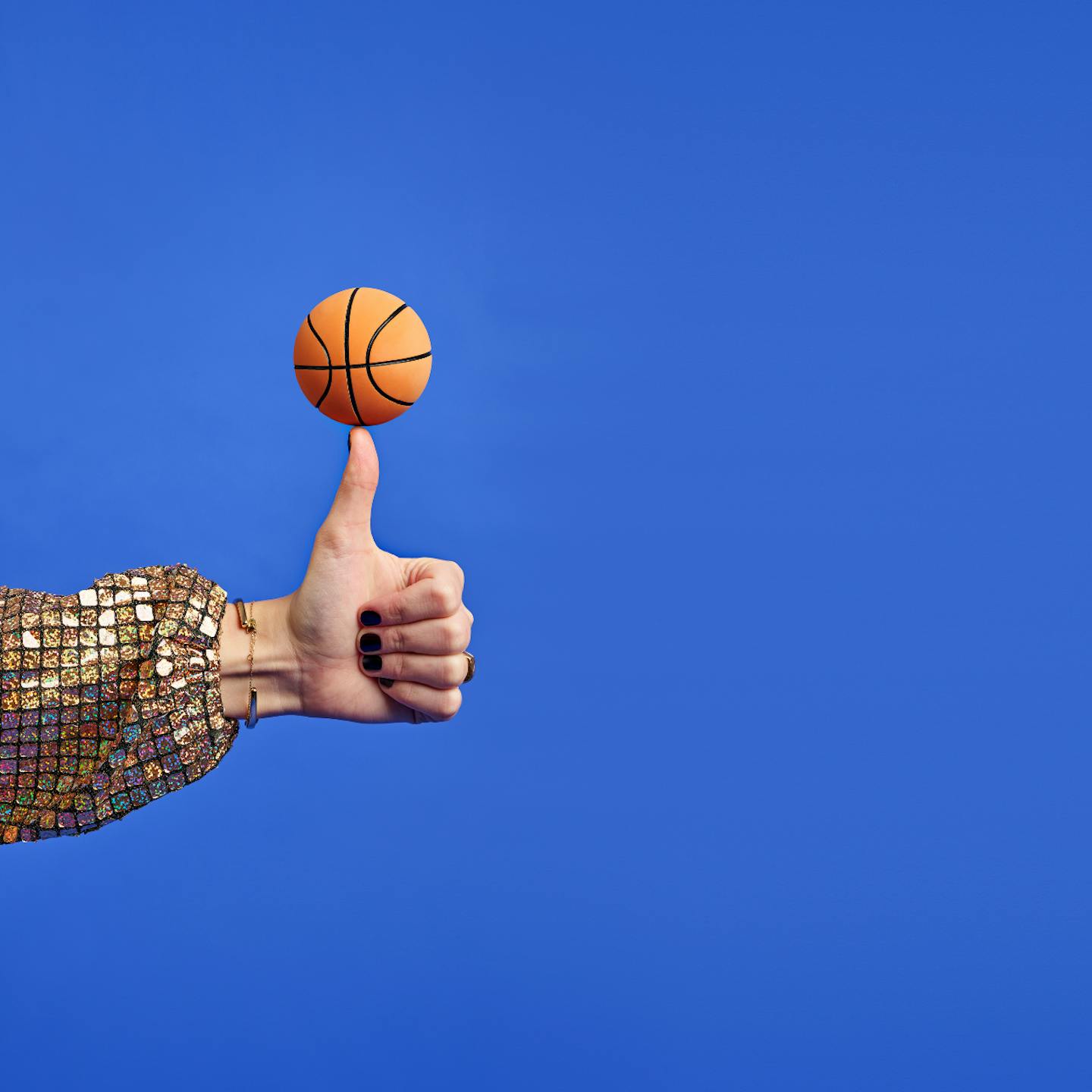 En lite basketboll som balanseras på en tumme. Blå bakgrund.