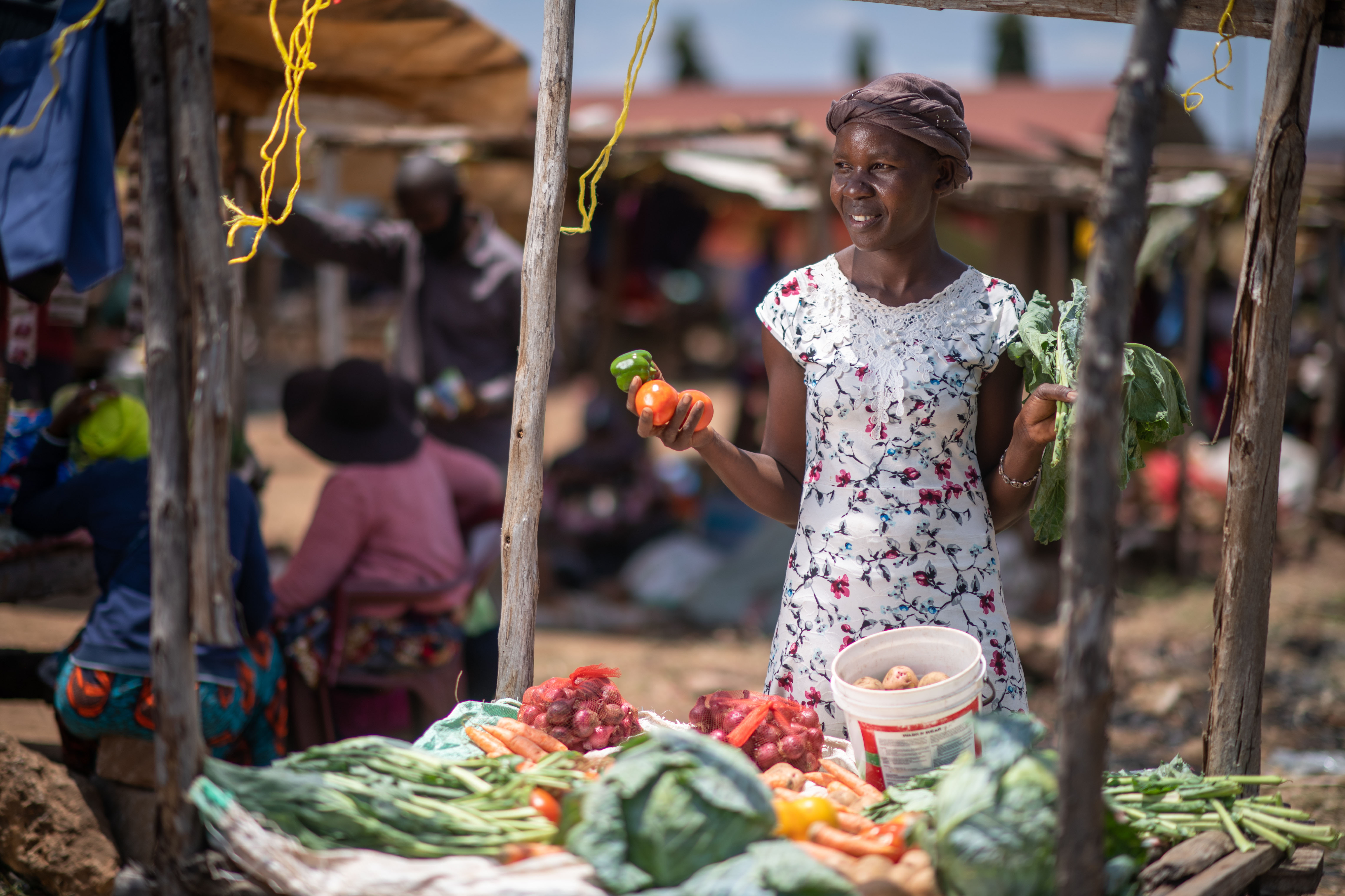 Picture of Agnes wearing a white, floral dress selling produce at a market.
