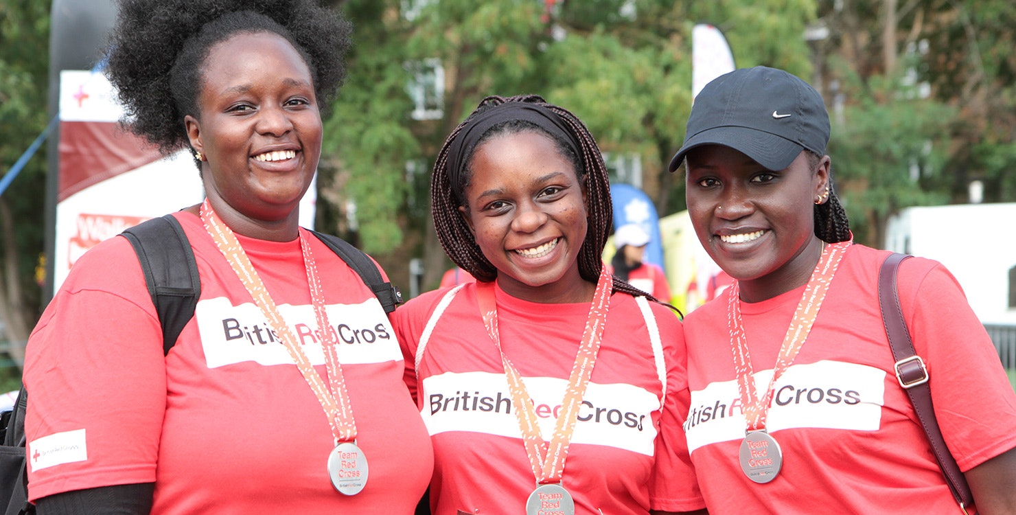 Three walkers in British Red Cross t-shirts stand at finish line of Walk for Humanity event. 
