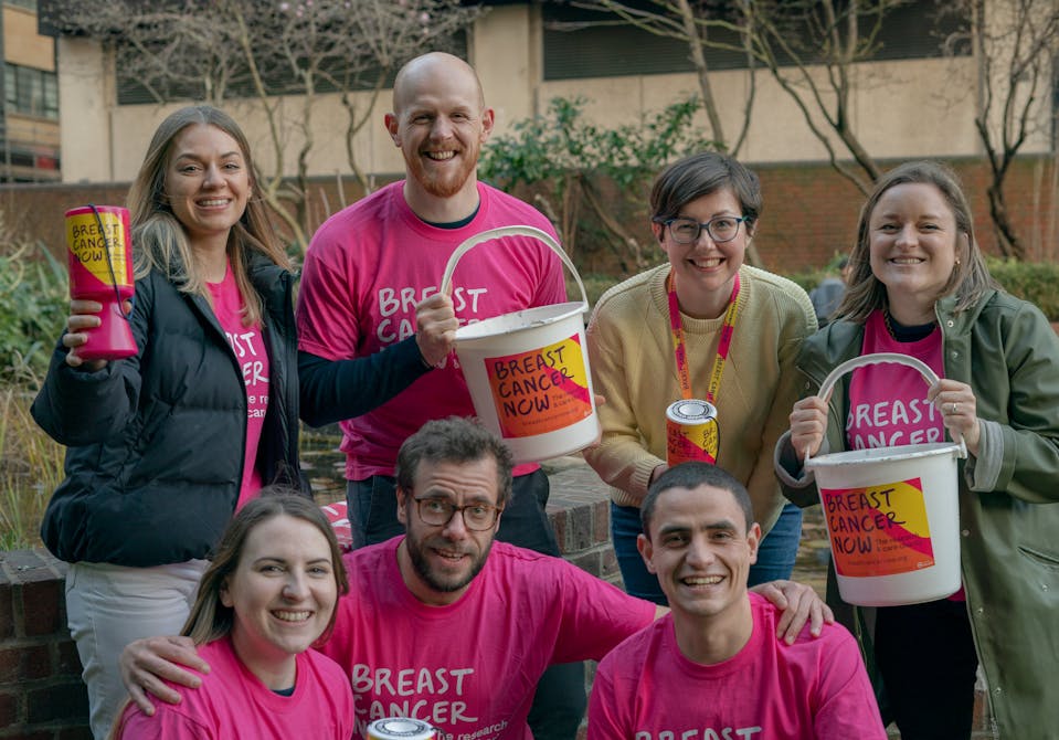 A group of people in pink Breast Cancer Now t-shirts holding donation buckets smiling at the camera