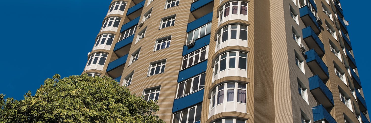 Facing bricks on an apartment building with blue balconies under a sunny blue sky