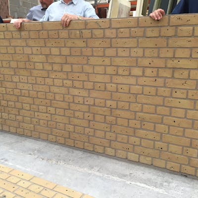 A group of men inspecting a GRP cladding panel that emulates a yellow brick built structure