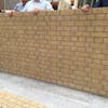 A group of men inspecting a GRP cladding panel that emulates a yellow brick built structure