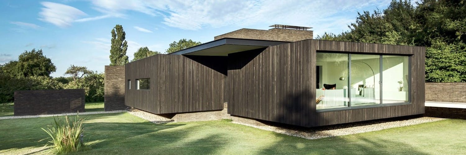A striking modern property clad in timber and brick set amongst trees and lawns