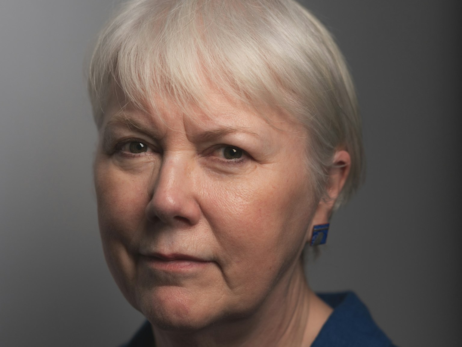 A professional headshot of Virginia Tandy. She has short grey hair and is wearing matching blue earrings and shirt.