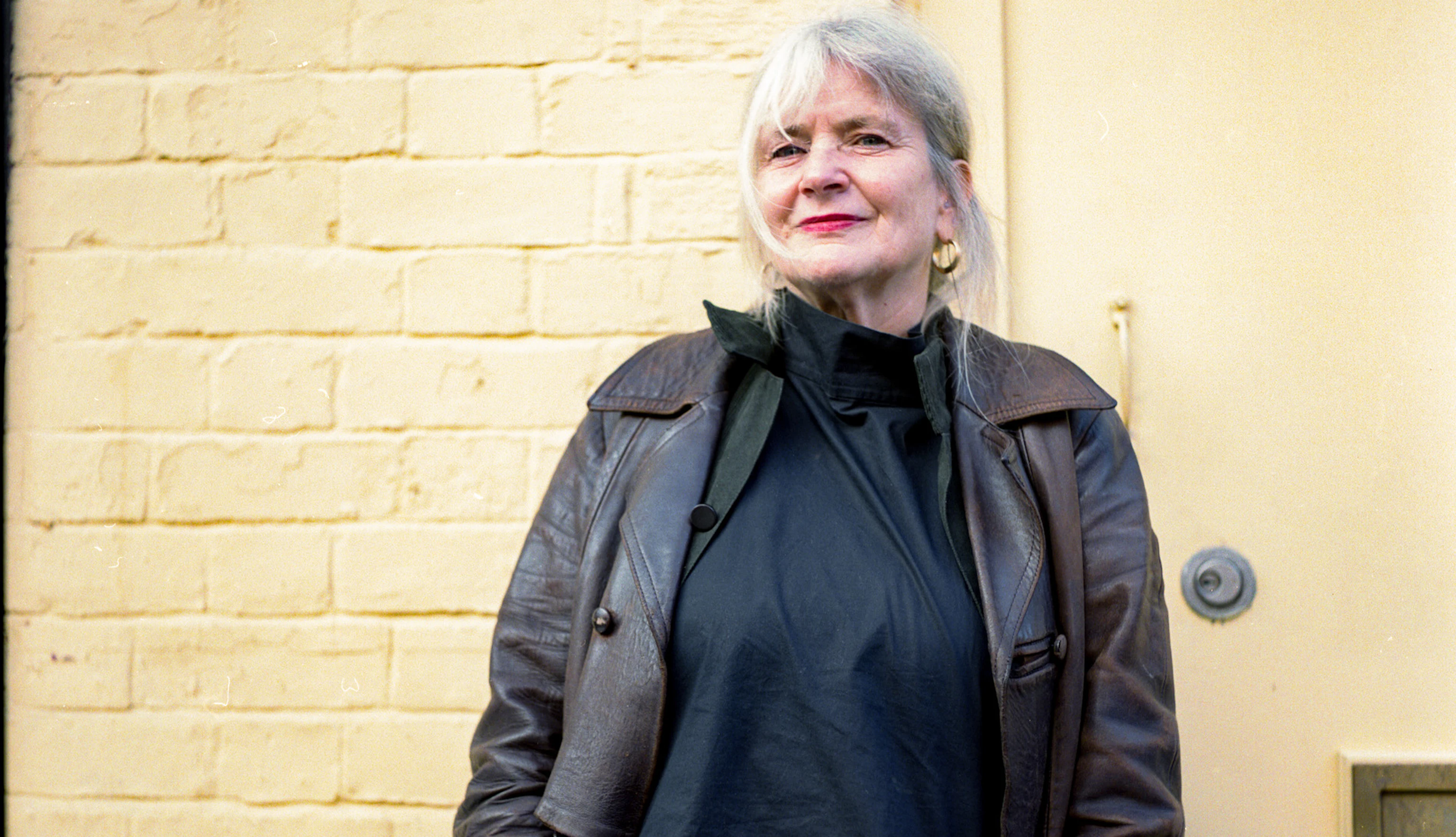 Debra smiles at the camera and is wearing a brown coat.