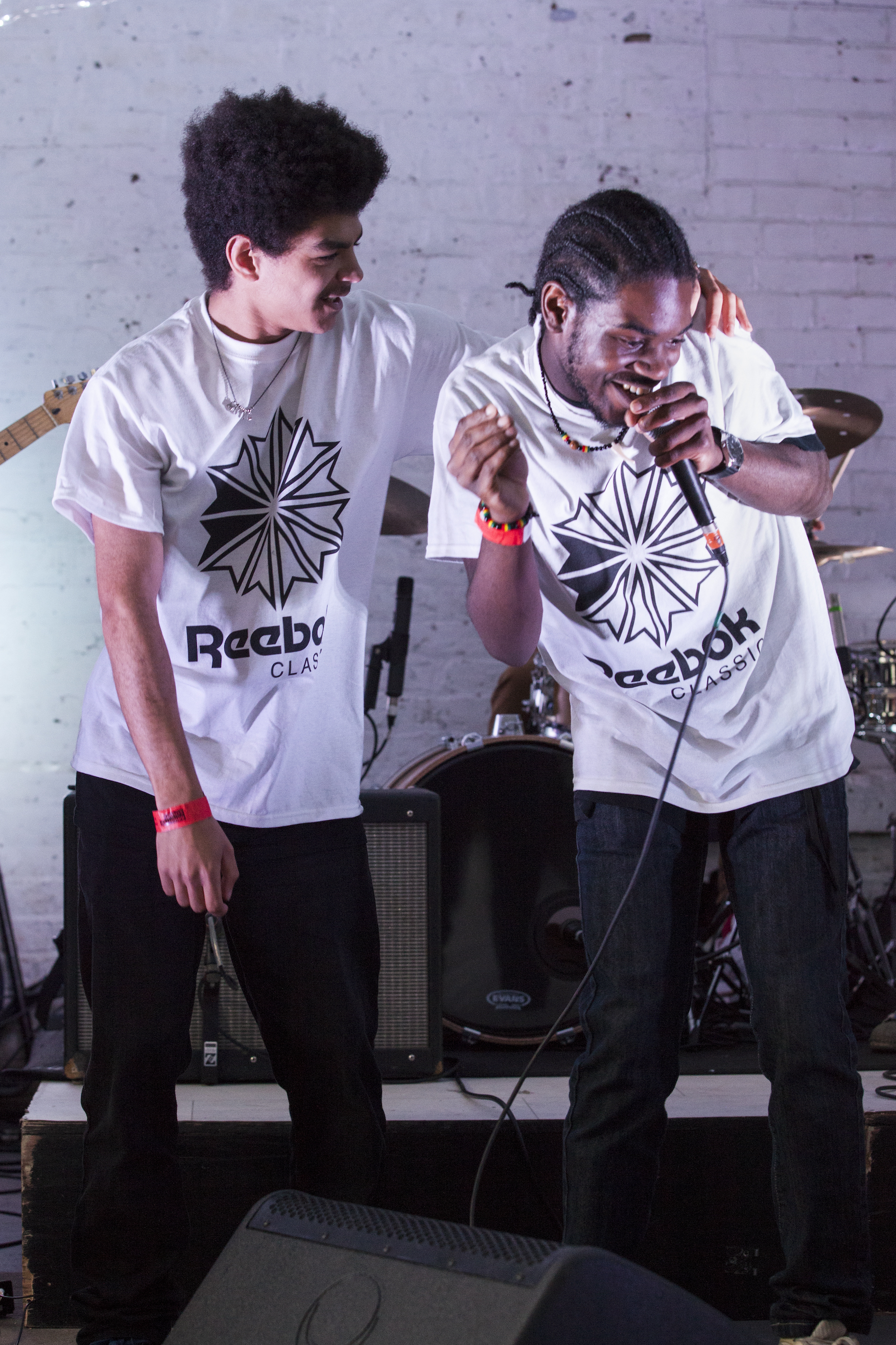 Close up shot of two participants on stage performing. One is singing into a microphone and the other is smiling with their arm around them.