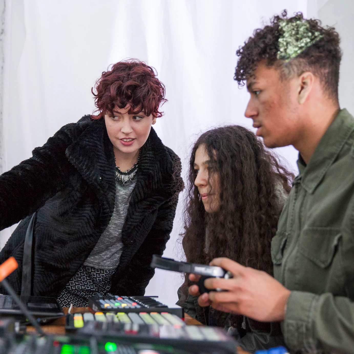 Two participants look at a laptop screen, the table is filled with production equipment. The facilitator is pointing to the screen.