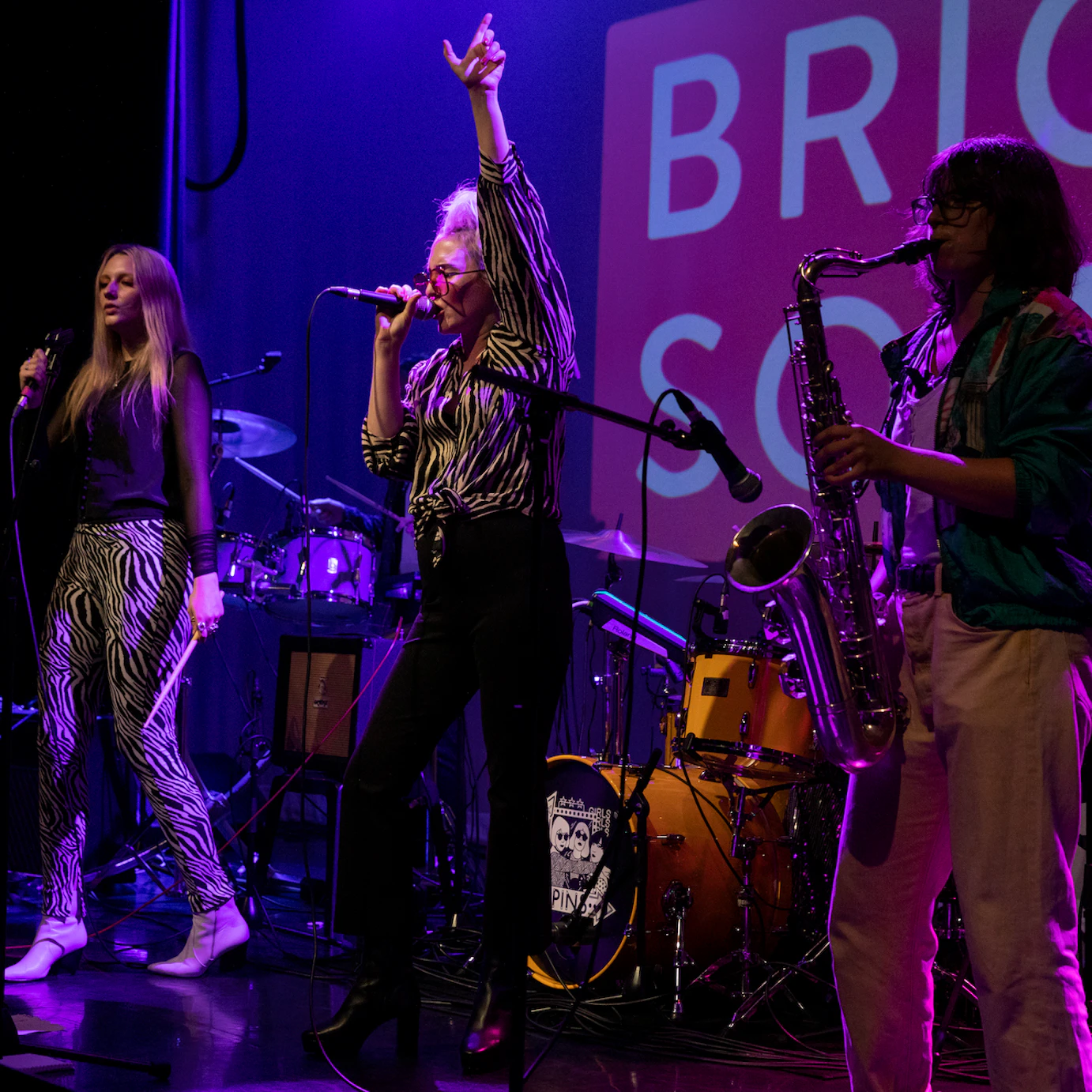 PINS' lead singer Faith playing on stage with musicians playing saxophone, guitars and vocals.