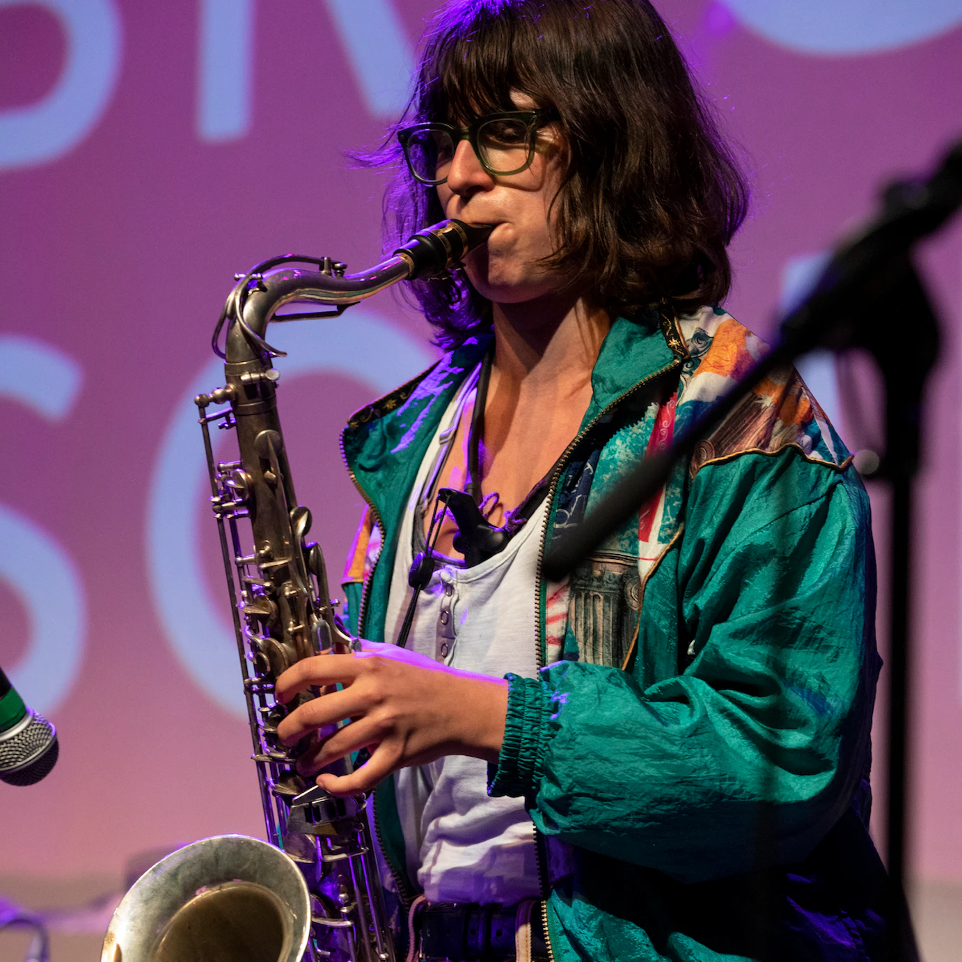 A saxophonist playing on stage dressed in a vintage green coat.