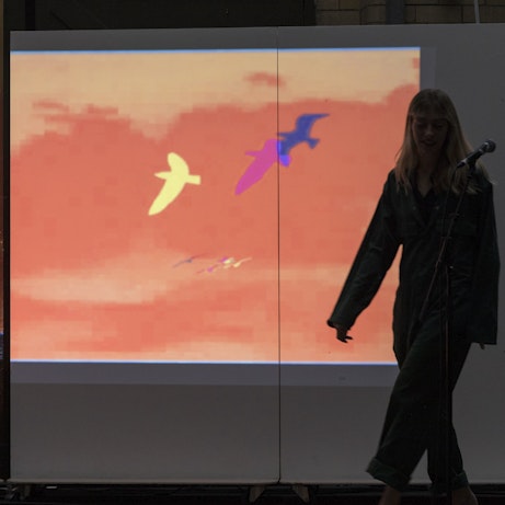 Three white monoliths joined together in a row, on which is projected animation of colourful silhouetted birds in an orange sky.