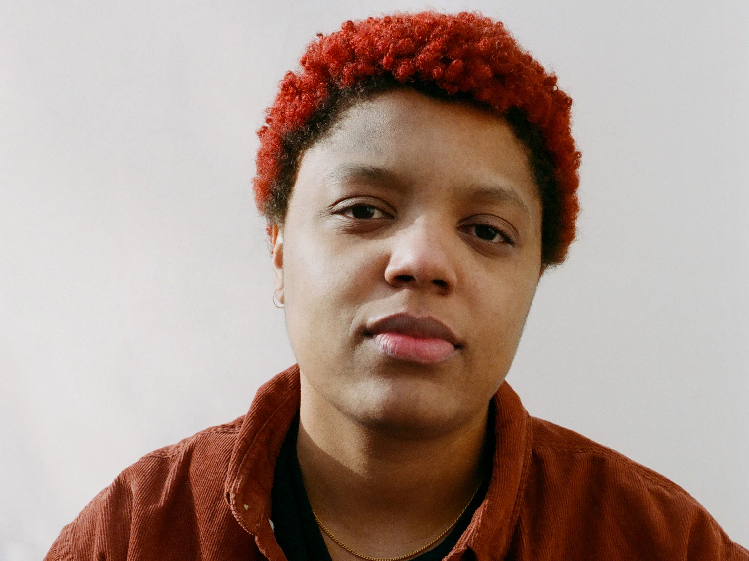 Loraine James in a red shirt in front of a white wall.