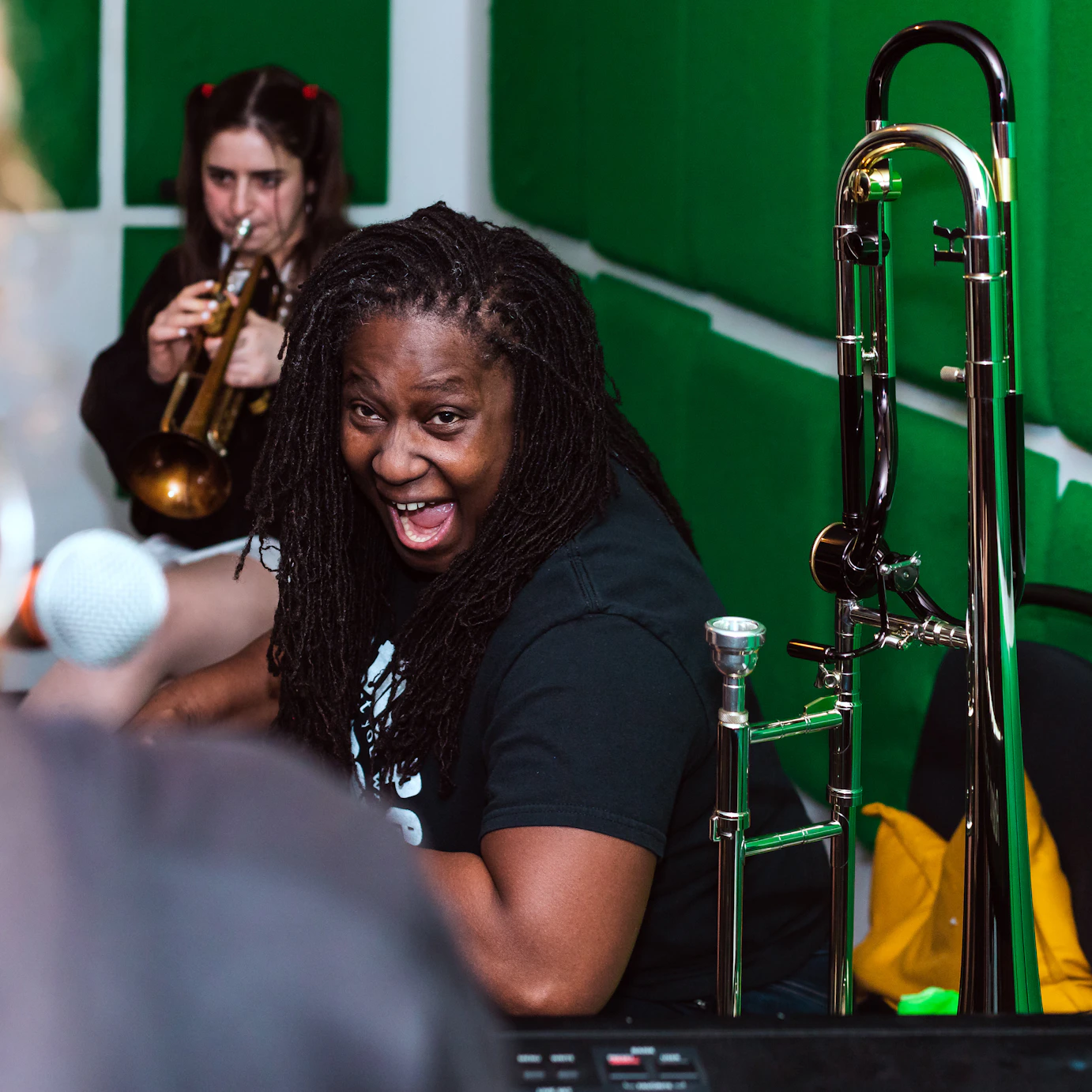 Hannabiell Sanders laughing in a music studio. Fee behind her is playing a trumpet.