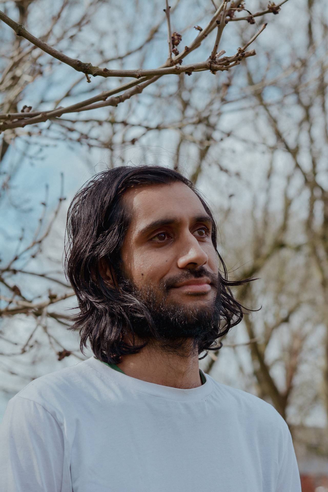 Balraj Samrai smiling into the distance. Behind him are blurred out, leafless branches.