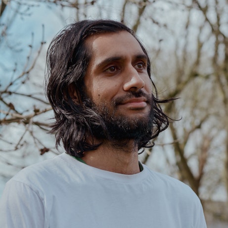 Balraj Samrai smiling into the distance. Behind him are blurred out, leafless branches.