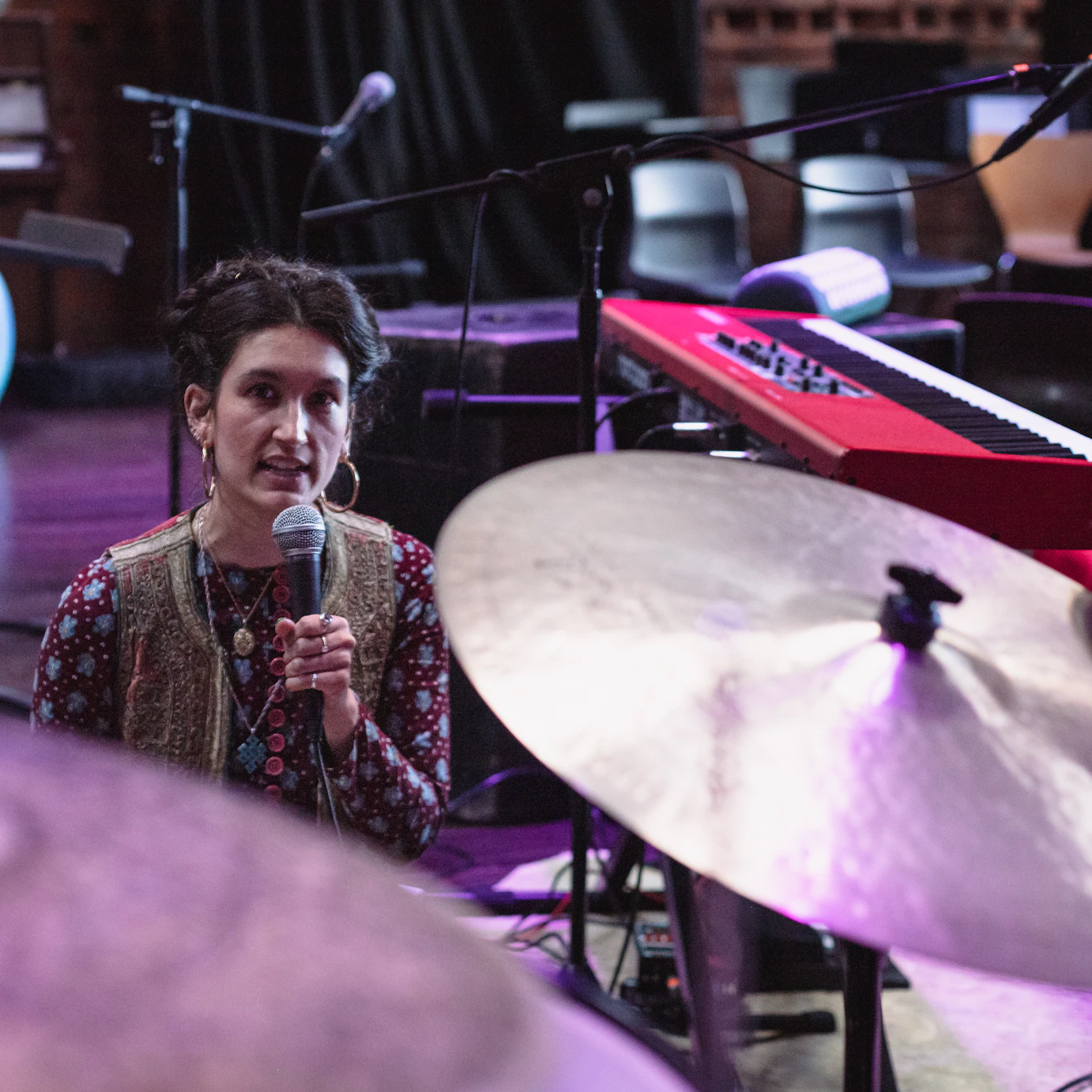 Mother Sugar sat amidst drums, keyboards and microphone stands speaking into a microphone.